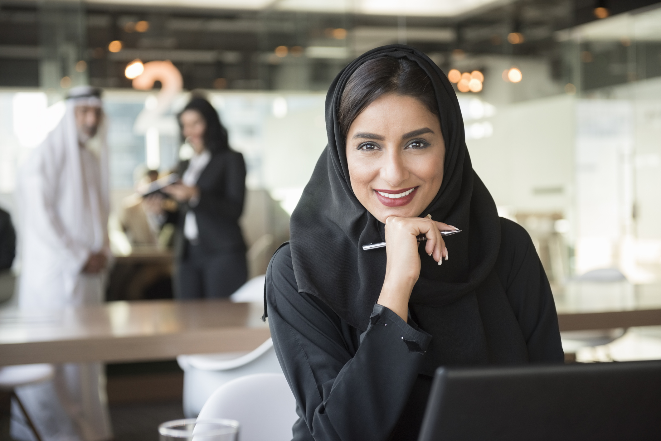 Smiling Arab businesswoman holding pen in office